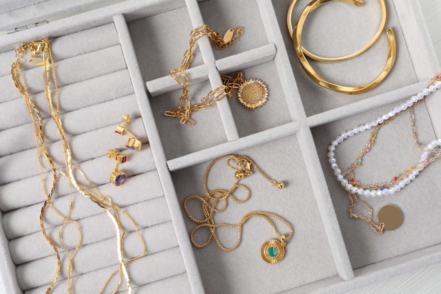 Sélection de bijoux dorés, colliers et boucles d'oreilles colorées rangés dans un coffret en velours gris