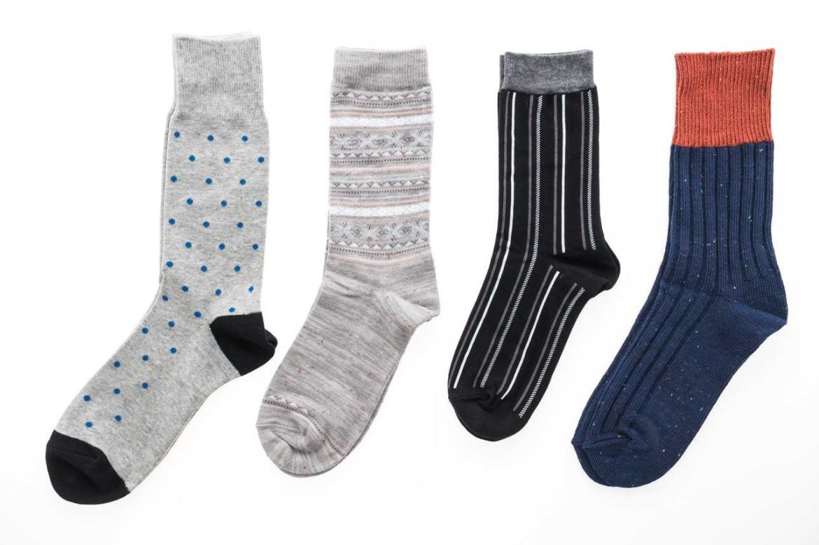 Quatre paires de chaussettes homme luxe aux motifs variés (pois, rayures, uni bicolore) alignées sur fond blanc.