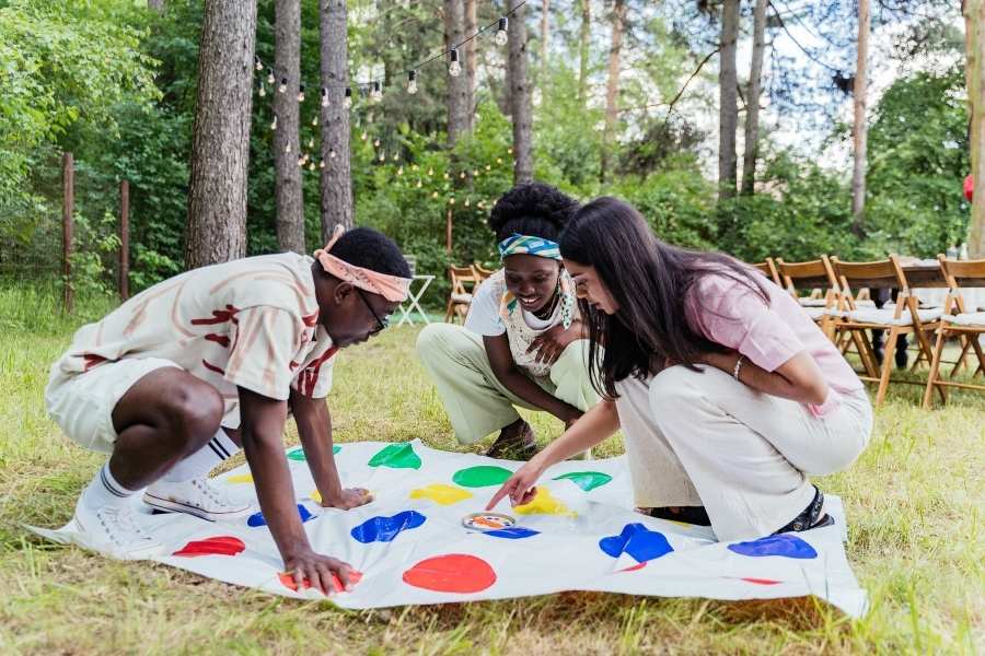 Trois amis jouent joyeusement au Twister sur une pelouse, illustrant parfaitement les jeux d'extérieur.